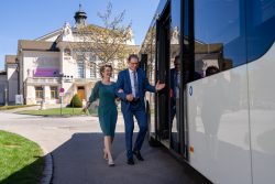 Ein elegant gekleidetes Paar steigt lächelnd in einen Bus von KMG Klagenfurt Mobil vor dem Stadttheater Klagenfurt ein.